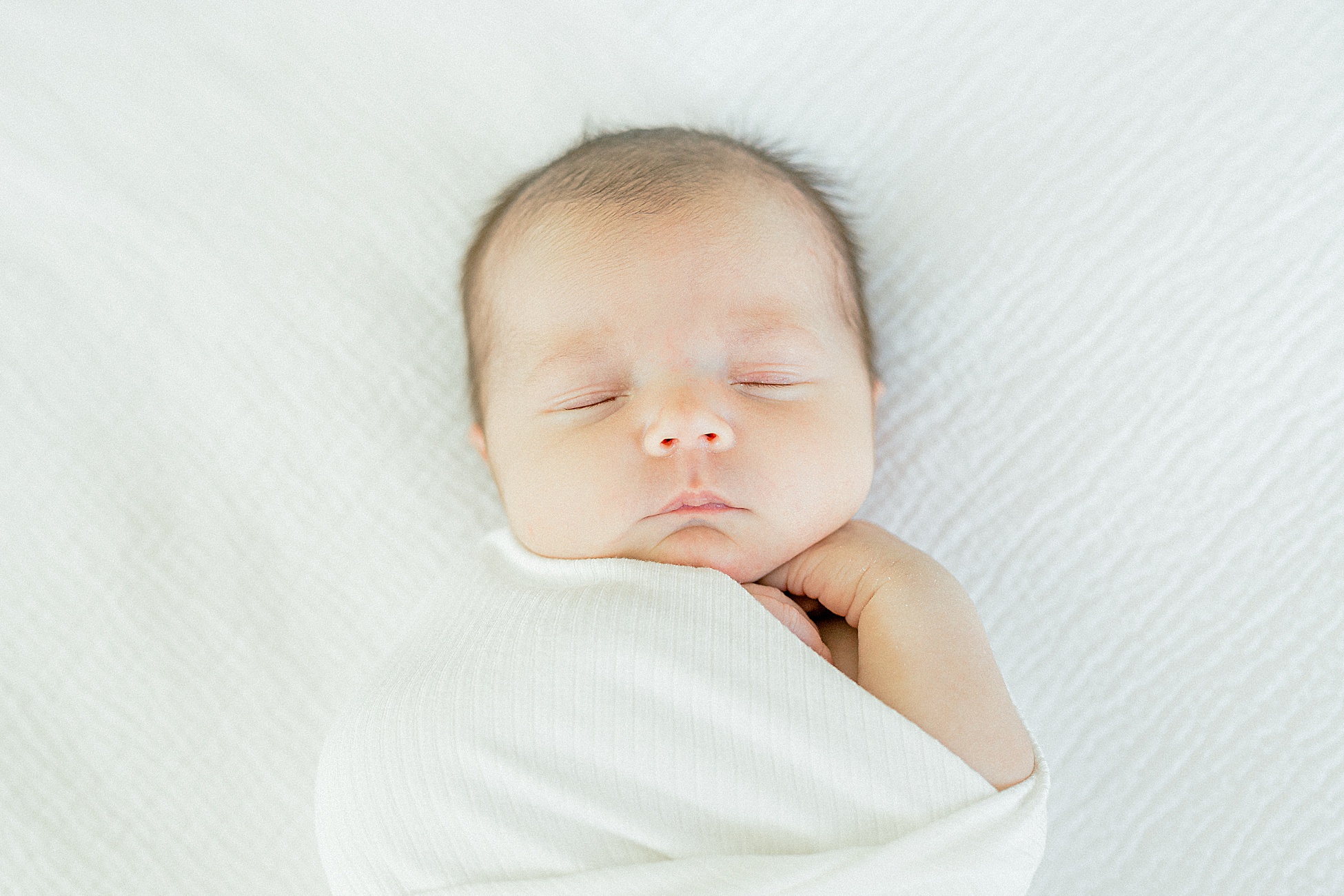 newborn baby girl wrapped in white blanket sleeping on bed