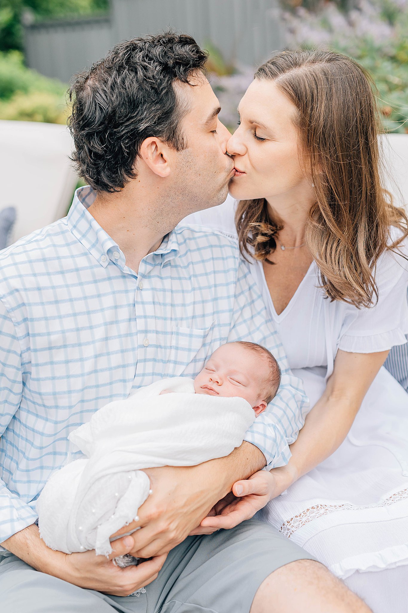 Outdoor newborn photos with momma and dad holding baby while kissing. 