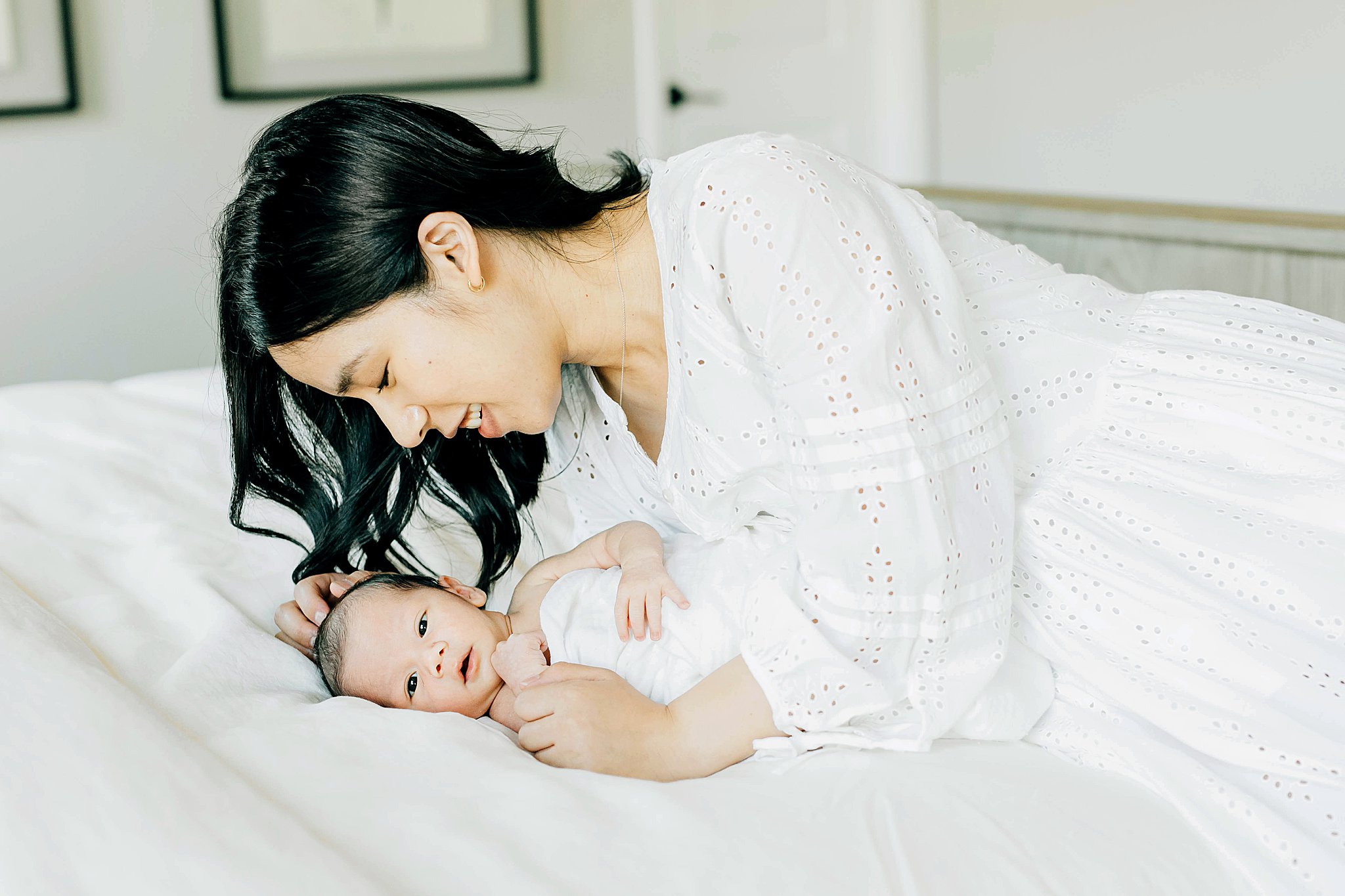 Mom and newborn on bed, with mom wearing long dress for outfit for newborn photos. 