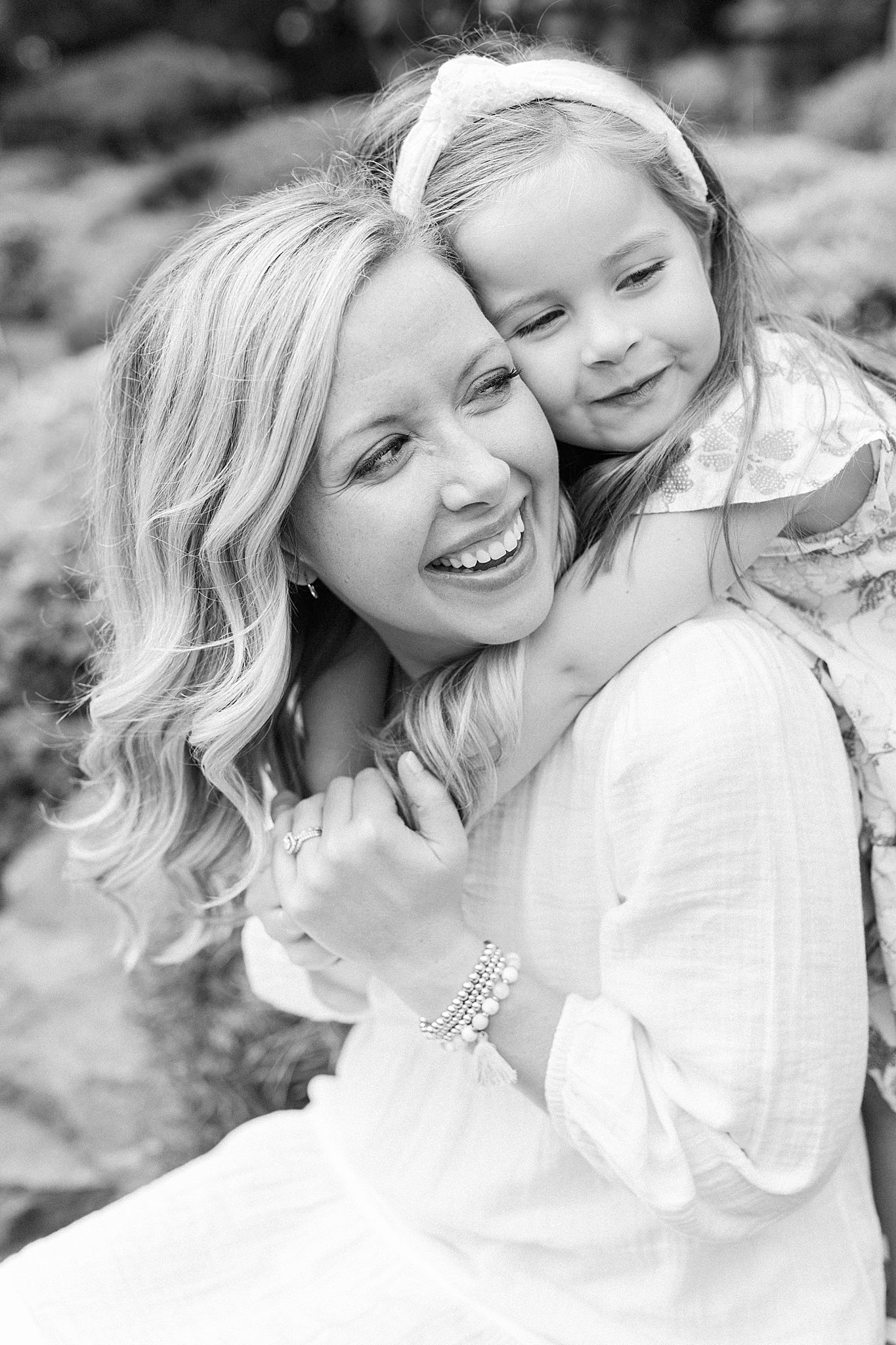 Mom and daughter smiling and hugging during outdoor family pictures.
