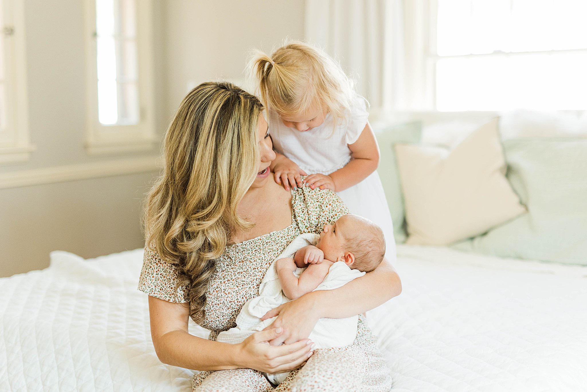 Mom holding baby while toddler looks at baby during MN newborn photographer session.