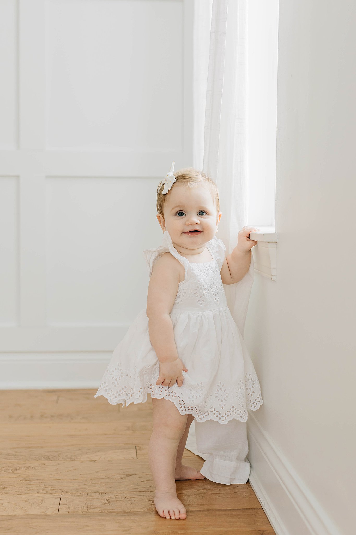 Baby standing and smiling during one year milestone portraits.
