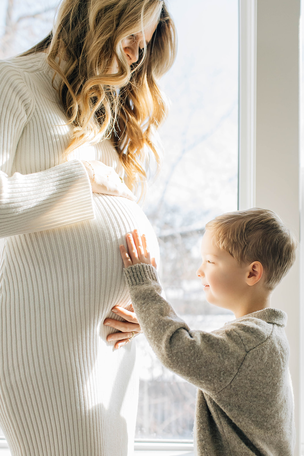 Boy Touching Moms Pregnant Belly with Sunlight Enveloping Them