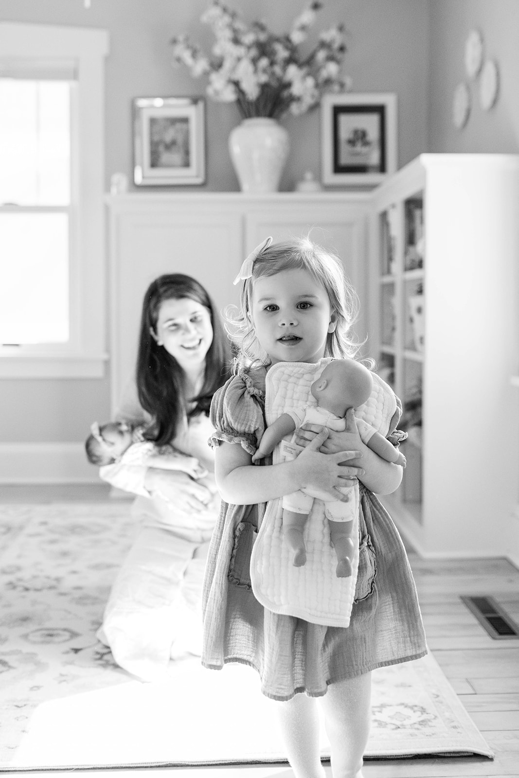 Toddler Holding Baby Doll During Photoshoot with Newborn Sibling