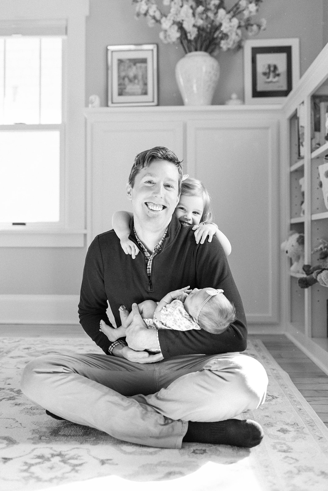 Dad Holds Newborn Baby with Toddler Child on His Back