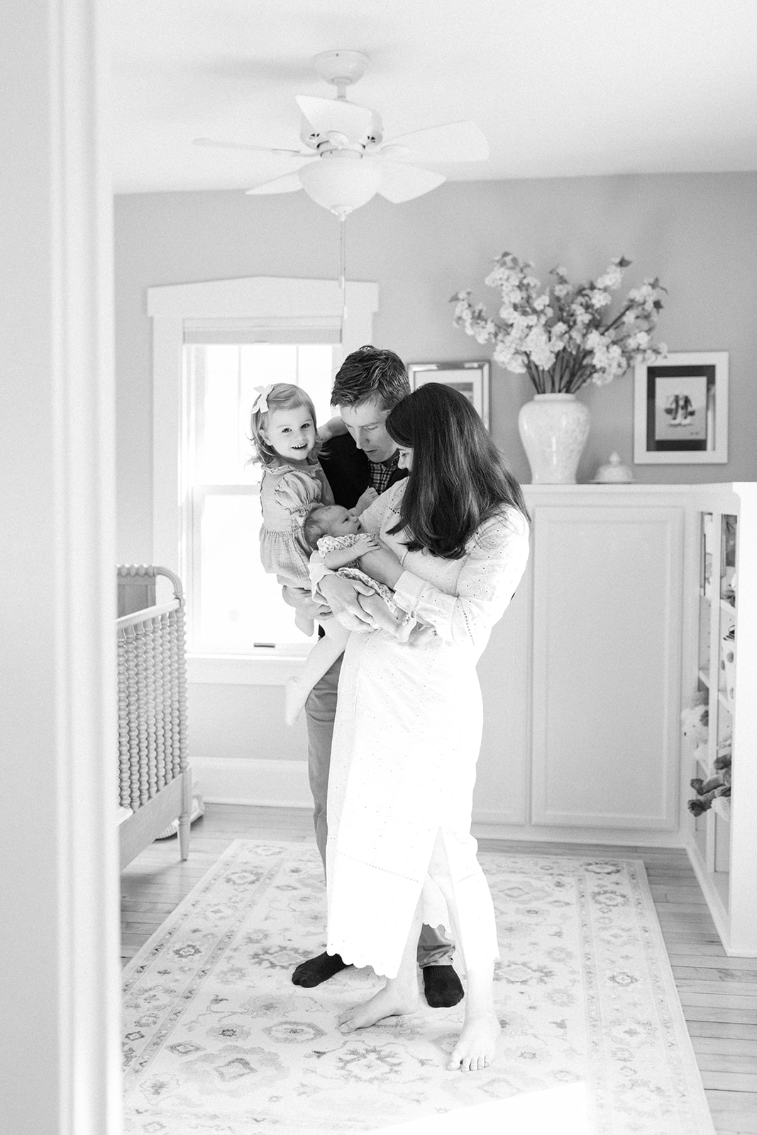 Black and White Photo of Family of Four Holding Newborn in Nursery